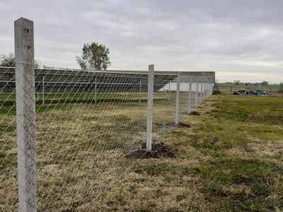 drótkerítés, mely elkeríti a napelemeket és a gazdasági épületet egy borongós tavaszi napon