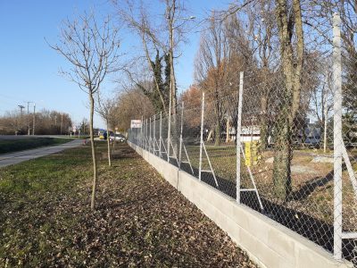Magasított alapzaton lévő drótkerítés késő őszi időben egy főút mellett